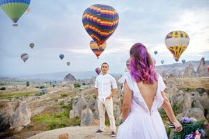 Couple in love stands on background of balloons in Cappadocia. Man and a woman on hill look at a large number of flying balloons. Turkey