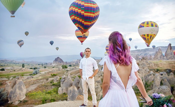 Couple in love stands on background of balloons in Cappadocia. Man and a woman on hill look at a large number of flying balloons. Turkey