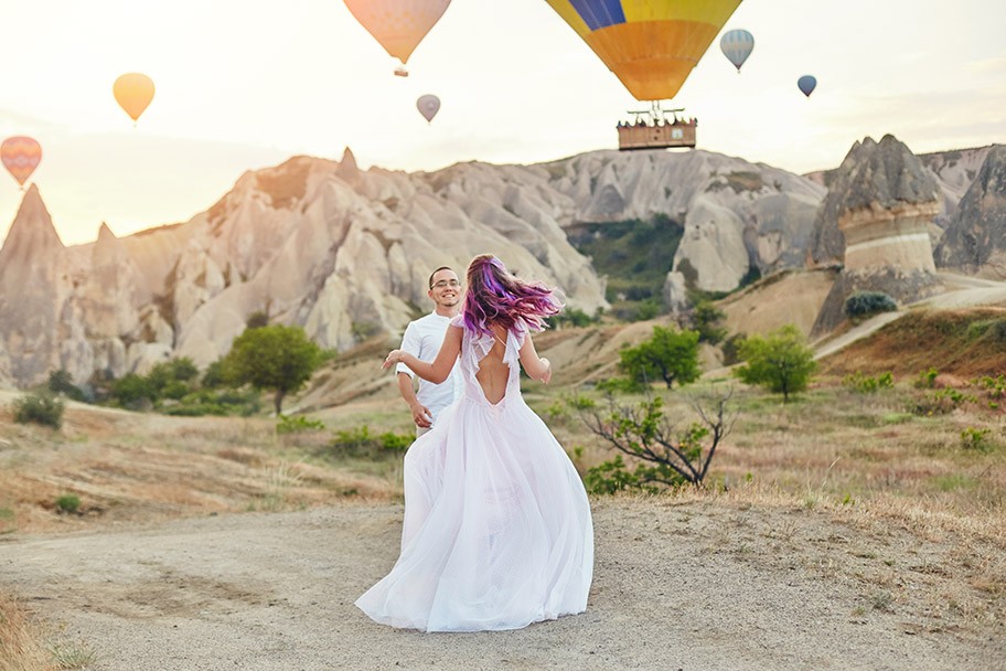 Couple in love stands on background of balloons in Cappadocia. Man and a woman on hill look at a large number of flying balloons. Turkey Cappadocia fairytale scenery of mountains. Wedding on nature